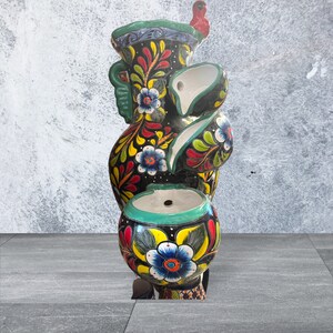 Puede incluir: Fuente de cer&aacute;mica pintada a mano de varios niveles. La fuente presenta una base negra con dise&ntilde;os florales coloridos en amarillo, rojo y azul. Tiene un borde turquesa y un p&aacute;jaro rojo en la parte superior. Es una pieza decorativa.