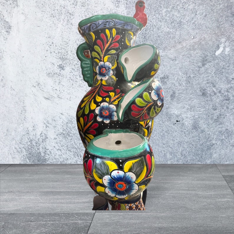 Puede incluir: Fuente de cer&aacute;mica pintada a mano de varios niveles. La fuente presenta una base negra con dise&ntilde;os florales coloridos en amarillo, rojo y azul. Tiene un borde turquesa y un p&aacute;jaro rojo en la parte superior. Es una pieza decorativa.