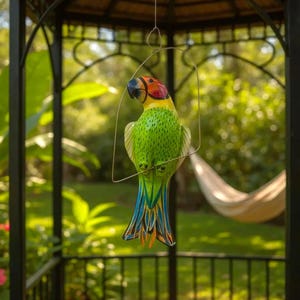 May include: A vibrantly painted wooden parrot sculpture, suspended by a wire frame. The parrot features a green body, a colorful head with red, yellow, and orange hues, and a tail with blue, yellow, and orange feathers. The sculpture is hanging outdoors.