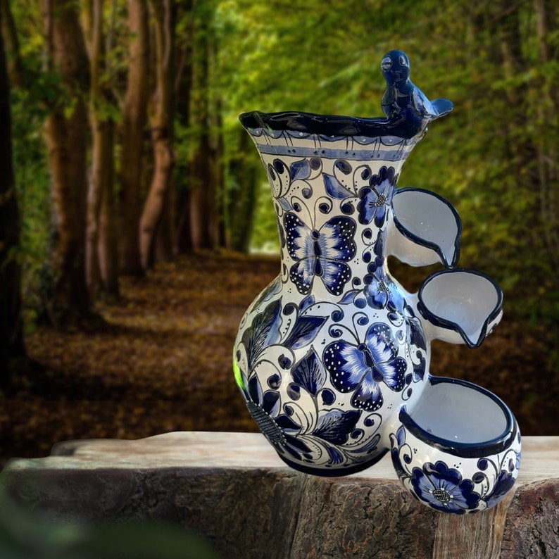 Puede incluir: Fuente de agua de cer&aacute;mica blanca y azul con dise&ntilde;o de mariposas y flores. La fuente tiene una figura de p&aacute;jaro en la parte superior y tres elementos de agua en cascada. La fuente mide unos 46 cm de altura.