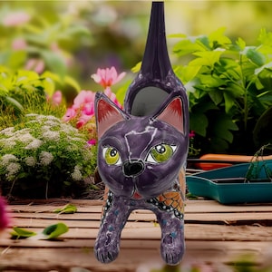 May include: A whimsical, purple cat-shaped planter with a tall, slender neck. The ceramic cat features green eyes, pink-lined ears, and butterfly wing designs. The planter is designed for outdoor use and adds a touch of artistic flair to any garden.