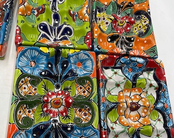 May include: A set of six colorful ceramic tiles with a floral design. The tiles are square and have a raised, textured surface. The flowers are painted in shades of blue, green, red, yellow, and orange.