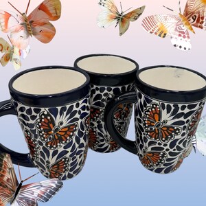 May include: Three blue and white ceramic mugs with butterfly designs. The mugs have a handle and are decorated with orange and black butterflies.