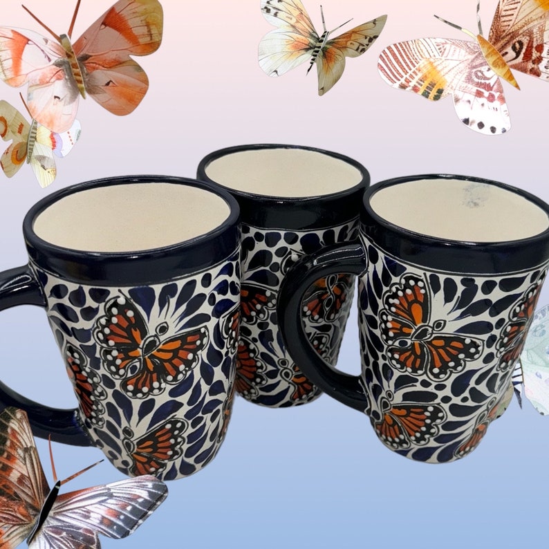 May include: Three blue and white ceramic mugs with butterfly designs. The mugs have a handle and are decorated with orange and black butterflies.