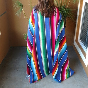 K&ouml;nnte beinhalten: Eine bunte gestreifte mexikanische Decke, auch Serape genannt, in Blaut&ouml;nen, Gr&uuml;n, Rot, Gelb und Orange. Die Decke ist in der H&auml;lfte gefaltet und &uuml;ber die Schultern einer Person gelegt.