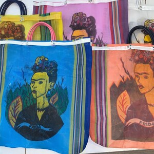 May include: Four colorful mesh tote bags with a Frida Kahlo portrait printed on each. The bags are striped in various colors, including blue, yellow, pink, and orange. Each bag has a white handle and the word "Frida" printed on the bottom.