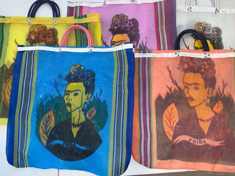 May include: Four colorful mesh tote bags with a Frida Kahlo portrait printed on each. The bags are striped in various colors, including blue, yellow, pink, and orange. Each bag has a white handle and the word "Frida" printed on the bottom.