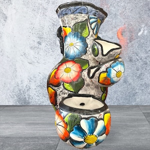 Puede incluir: Una maceta decorativa de cer&aacute;mica pintada a mano con un acabado gris moteado. La maceta presenta vibrantes dise&ntilde;os florales en rojo, azul, amarillo y naranja. Tiene m&uacute;ltiples aberturas para plantas y un borde negro.
