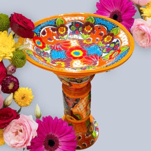 Könnte beinhalten: Eine lebendige, handbemalte Vogeltränke aus Keramik mit einem Sockel. Die Schale zeigt ein farbenfrohes Blumenmuster mit Orange-, Blau-, Rot- und Gelbtönen. Der Sockel ist ebenfalls mit ähnlichen Blumenmustern verziert. Ein dekoratives Gartenaccessoire.