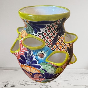 Może przedstawiać: Ceramiczna doniczka na truskawki z szerokim otworem i wieloma bocznymi kieszeniami z limonkową krawędzią. Zewnętrzna strona ozdobiona jest żywym, ręcznie malowanym wzorem kwiatowym i kratką w odcieniach ciemnego błękitu, pomarańczu i jasnej zieleni.