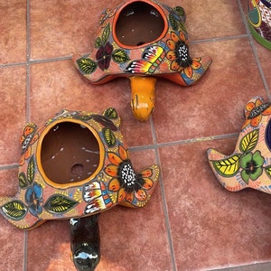 Pode incluir: Dois vasos de cerâmica em forma de tartaruga, pintados com flores e borboletas. Os vasos são de cor laranja, marrom, verde, amarelo, azul e preto.