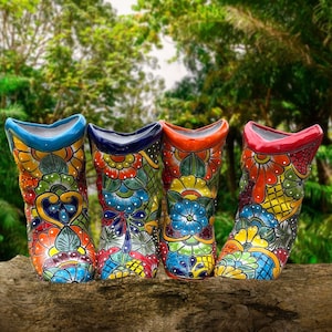 May include: Four colorful ceramic boots with floral patterns. The boots are painted in shades of blue, green, yellow, orange, and red. They are arranged in a row on a wooden surface.