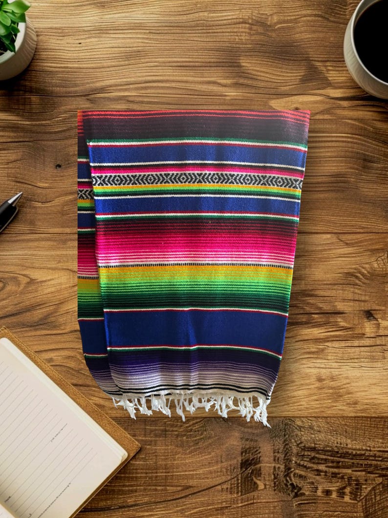 K&ouml;nnte beinhalten: Eine bunte mexikanische Decke mit Streifen in Rot, Rosa, Gr&uuml;n, Blau, Gelb und Wei&szlig;. Die Decke hat einen Fransenrand.