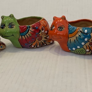 May include: Four colorful ceramic snail planters with painted floral designs. Each planter has a different color base and features a unique floral pattern.