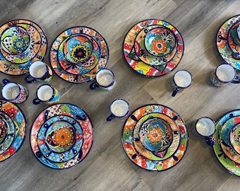May include: A set of colourful Mexican Talavera pottery dinnerware, including plates, bowls, and mugs. The dishes feature intricate floral designs in shades of blue, green, yellow, and orange, with a black outline.