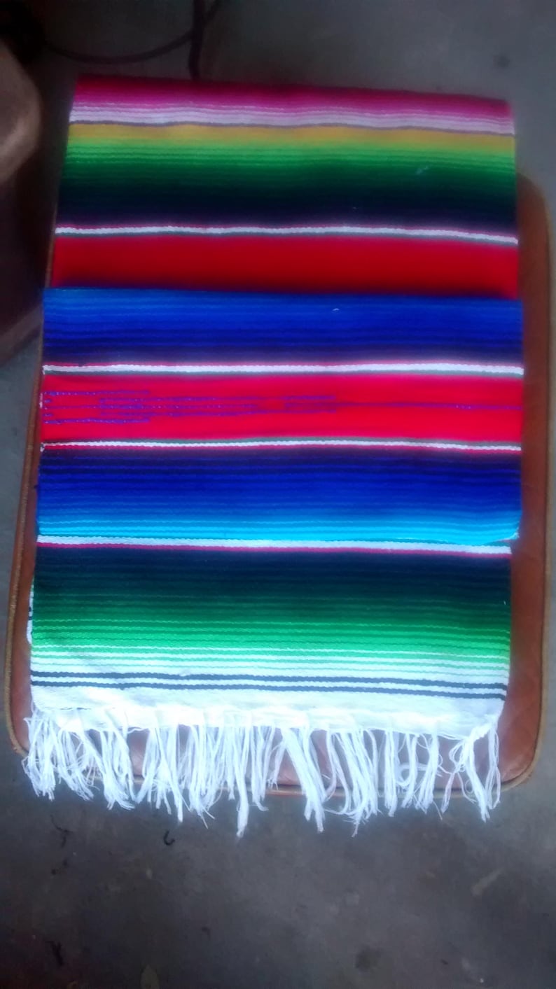 K&ouml;nnte beinhalten: Eine bunte mexikanische Decke mit wei&szlig;en Fransen. Die Decke hat Streifen in Rot, Gr&uuml;n, Blau, Gelb und Wei&szlig;.