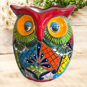 May include: A vibrant, hand-painted ceramic owl-shaped planter. The owl features a glossy red head and large orange eyes with blue accents. Its body is adorned with intricate patterns in blue, green, orange, and yellow, making it a colorful decorative piece.