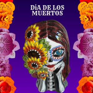 May include: A Day of the Dead ceramic skull figurine with sunflower and floral accents. The skull features painted details, including blue eyes, red lips, and a floral design. The text "Día de los Muertos" is at the top.