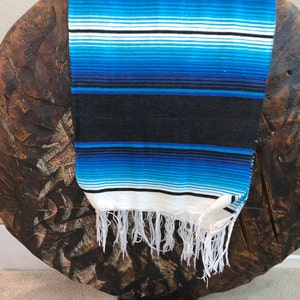 May include: A blue and white striped serape with black stripes and white fringe.