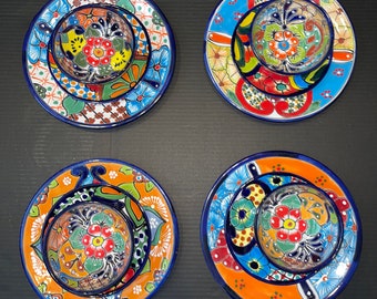 May include: Four colourful ceramic plates with intricate designs. Each plate features a smaller plate nested inside, creating a layered effect. The plates are decorated with vibrant floral patterns and blue accents.