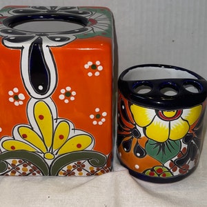 Peut inclure: Un ensemble orange en céramique comprenant un distributeur de mouchoirs et un porte-brosse à dents. Le distributeur de mouchoirs est carré avec un motif floral jaune, vert et blanc. Le porte-brosse à dents a trois trous.