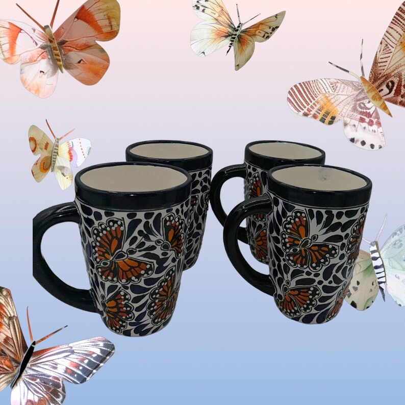 May include: Set of four ceramic mugs with a black rim and handle. Each mug features a white background with a blue and orange butterfly design.