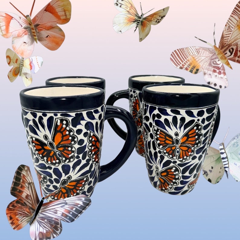 May include: Set of four blue and white ceramic mugs with a butterfly design. Each mug features a different butterfly with orange and black wings. The mugs have a handle and are perfect for coffee, tea, or hot chocolate.