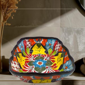 May include: A colorful ceramic serving bowl with a square shape and a scalloped edge. The bowl is decorated with a floral pattern in shades of yellow, red, blue, green, and white.