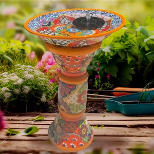 Könnte beinhalten: Ein lebendiges, handbemaltes Vogelbad aus Keramik mit Solarbrunnen. Das Vogelbad hat ein farbenfrohes Blumendesign mit orangefarbenen, blauen und roten Akzenten. Der Sockel hat ein Sockeldesign, und die Schale ist breit und flach.