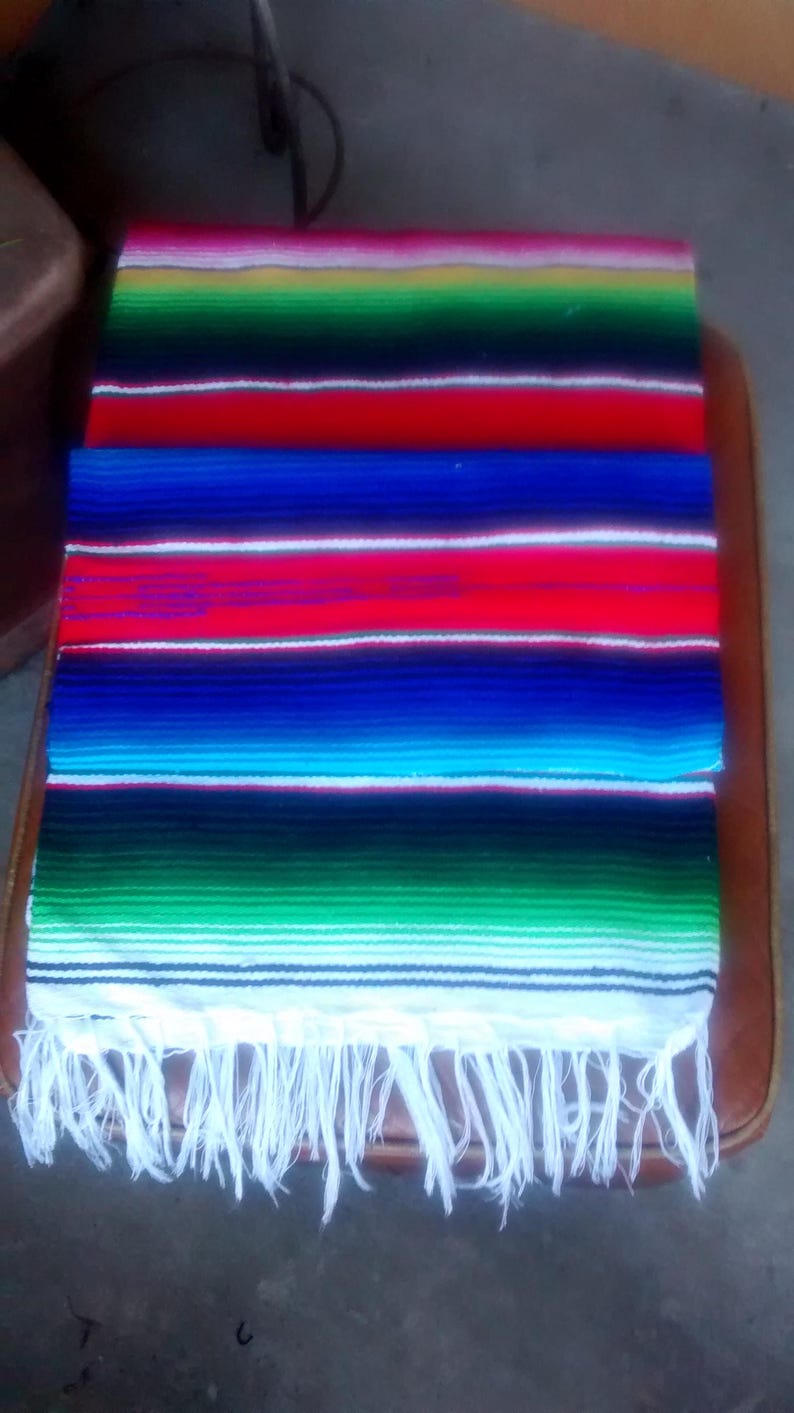 K&ouml;nnte beinhalten: Eine bunte mexikanische Decke mit einem wei&szlig;en Fransenbesatz. Die Decke hat Streifen in Rot, Blau, Gr&uuml;n, Gelb und Wei&szlig;.