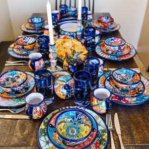 Puede incluir: Una mesa puesta con vajilla de cerámica mexicana Talavera colorida, cuencos, tazas y vasos. Los platos presentan intrincados patrones florales en tonos azules, verdes, amarillos y rojos.