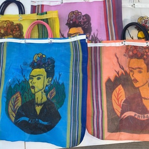 May include: Four colorful mesh tote bags with a Frida Kahlo design. Each bag features a different color background and a portrait of Frida Kahlo with flowers in her hair. The bags have white straps and the word "Frida" printed on them.
