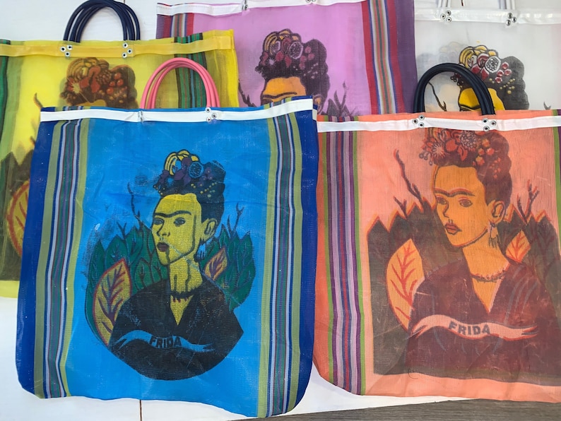 May include: Four colorful mesh tote bags with a Frida Kahlo design. Each bag features a different color background and a portrait of Frida Kahlo with flowers in her hair. The bags have white straps and the word "Frida" printed on them.