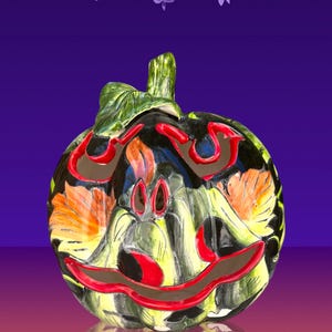May include: A ceramic pumpkin with a carved face, painted in black, green, red, and orange. The pumpkin has a stem and leaf detail. The design is reminiscent of a jack-o'-lantern, perfect for Halloween decorations.