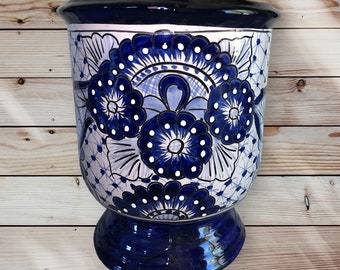 Può includere: Una fioriera in ceramica con base a piedistallo, caratterizzata da un motivo floreale dipinto a mano nei toni del blu e del bianco. La fioriera ha un bordo e una base blu scuro, con motivi e dettagli intricati. Un pezzo decorativo.