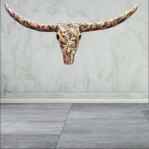 May include: A decorative longhorn skull with a copper finish and detailed black floral patterns. The skull is mounted on a wall, highlighting its intricate design. This piece is a unique home decor item, suitable for adding a rustic touch.