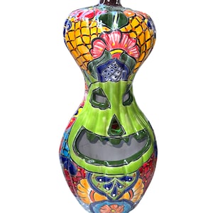 May include: A ceramic pumpkin with a green face and colorful floral designs. The pumpkin is painted in shades of yellow, orange, red, blue, green, and white.