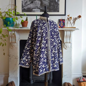 Könnte beinhalten: Eine marineblaue bestickte Jacke mit weißen Blumenmustern. Die Jacke befindet sich auf einem Mannequin vor einem Kamin.