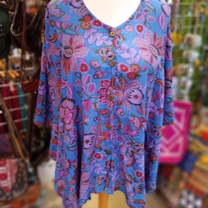 May include: A blue and purple floral print tunic with a button-up front. The tunic has a loose, flowing fit and a slightly asymmetrical hemline.