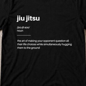 May include: A black short-sleeved t-shirt featuring white text that defines jiu jitsu as the art of making your opponent question all their life choices while simultaneously hugging them to the ground, accompanied by a white martial arts belt.
