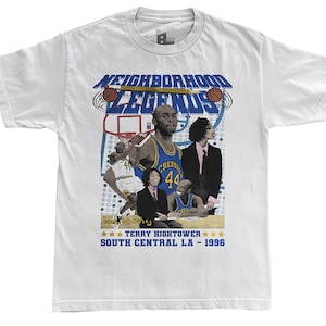 Puede incluir: Camiseta blanca con un diseño gráfico que presenta el texto "NEIGHBORHOOD LEGENDS" e imágenes de baloncesto. El diseño incluye imágenes de jugadores de baloncesto y el texto "TERRY HIGHTOWER SOUTH CENTRAL LA - 1996".