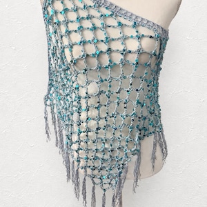 May include: A one-shoulder crochet shawl featuring a light gray yarn base with an open net pattern. The garment is embellished with small, shimmering turquoise sequins throughout the mesh structure and finished with long, thin fringe along the bottom edge.