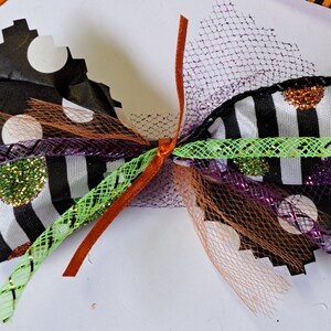 May include: A black and white striped ribbon with white polka dots and orange glitter, tied with a green and purple ribbon, and a brown ribbon. The ribbon is decorated with black and white netting.