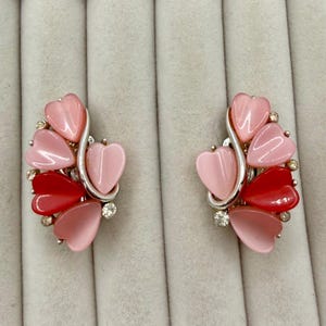 May include: A pair of vintage clip-on earrings. Each earring features a cluster of heart-shaped stones in shades of pink and red, accented with small clear crystals and a silver-tone metal design.