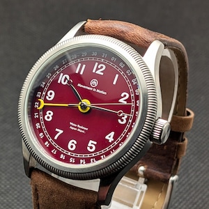 May include: A wristwatch with a burgundy dial and a brown leather strap. The watch face features white numerals, a yellow second hand, and the text "Movement in Motion". The watch has a stainless steel case and a brown leather strap.