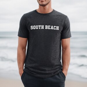 May include: A dark heather grey t-shirt with the text "SOUTH BEACH" printed in white.