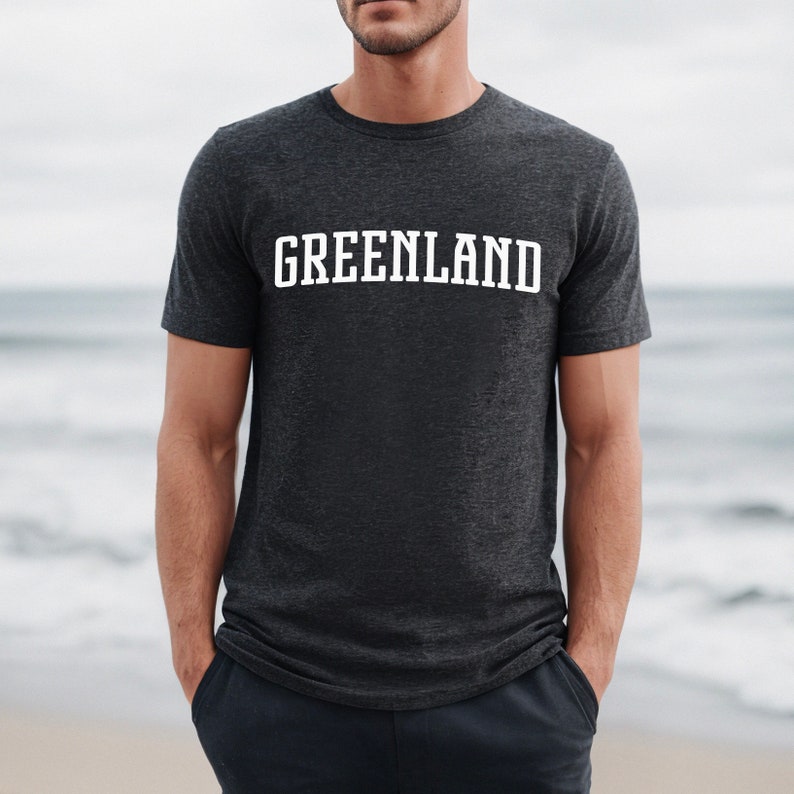 May include: A dark heather grey t-shirt with the word "GREENLAND" printed in white on the front.