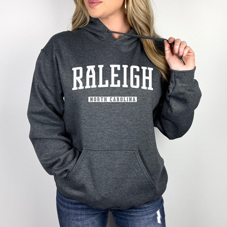 Peut inclure: Un sweat &agrave; capuche gris fonc&eacute; avec le texte "RALEIGH NORTH CAROLINA" en blanc.