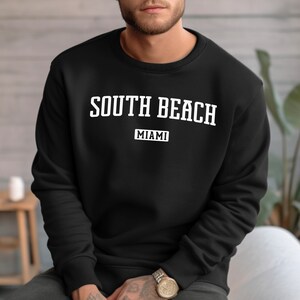 May include: Black sweatshirt with white text that reads "SOUTH BEACH MIAMI" in a vintage collegiate style font.