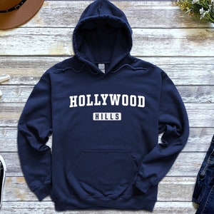 May include: A navy blue hooded sweatshirt with the text "HOLLYWOOD HILLS" in white.